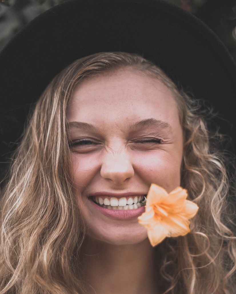 Nicole, a blond girl, is smiling and holding a flower in her mouth.
