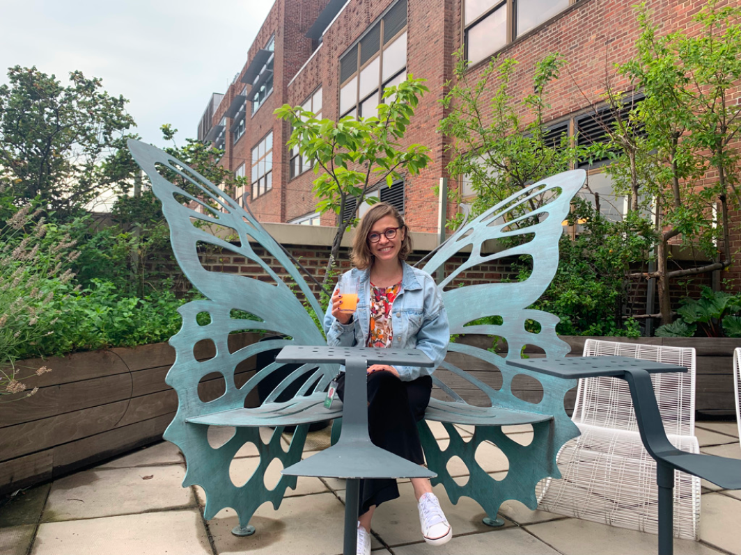 aira sitting on a butterfly-shaped bench with a drink in her hand, surrounded by greenery.